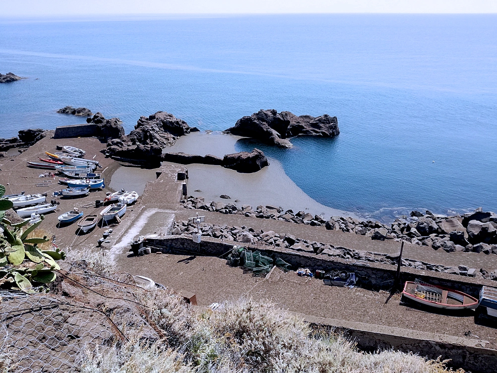 Il Porto di Ginostra il giorno dopo il parossisma del 3 luglio 2019. I depositi di ricaduta dei prodotti piroclastici emessi durante l'eruzione (scorie, pomici e lapilli marrone chiaro) si riconoscono sul molo e sulle barche tirate in secco. Parte di questi forma una coltre che galleggia nella piccola baia (foto Gianfilippo de Astis). - Uno - Galleria